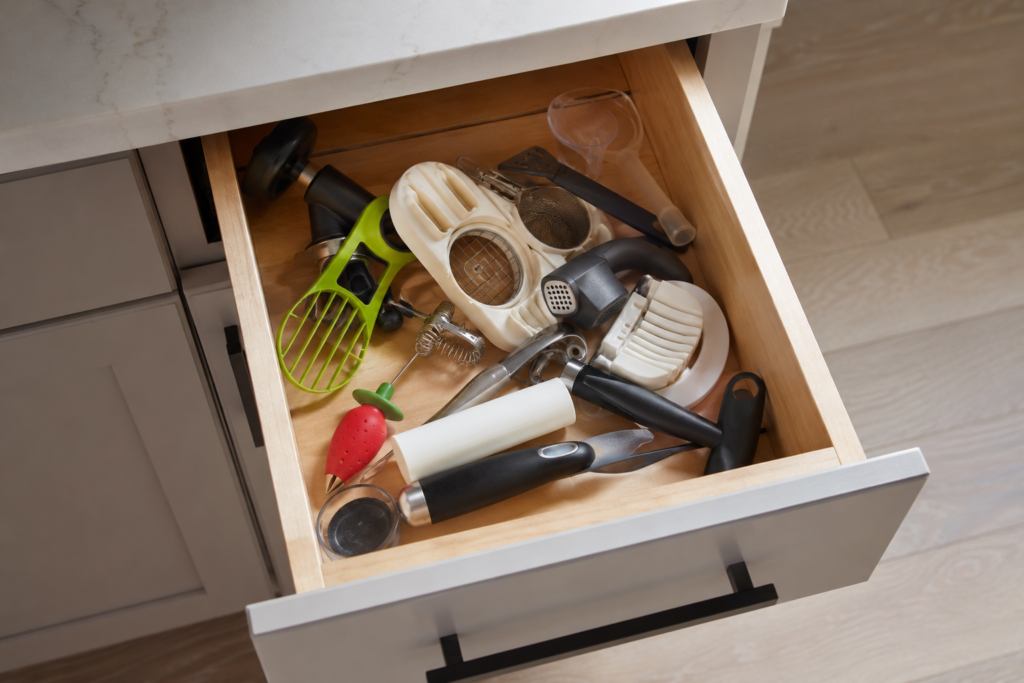 Cluttered kitchen junk drawer filled with unused gadgets like an avocado slicer and egg cuber